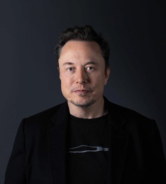 A portrait photo of Elon Musk wearing a black t-shirt and dark blazer against a dark gray background.