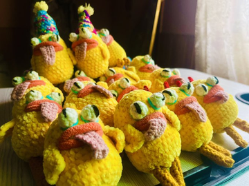 A collection of hand-crocheted yellow duck amigurumi figures wearing colorful party hats and scarves, displayed together in a cluster with small crocheted accessories.