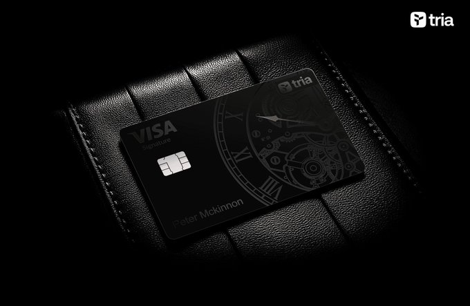 A black Tria Visa Signature credit card with a watch movement design and the name 'Peter McKinnon', displayed on black leather.