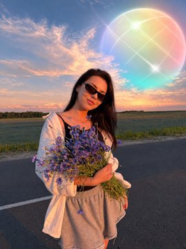 A woman in sunglasses stands on a road at sunset holding a bouquet of lavender, with a glowing multicolored sphere floating above her. The image symbolically reflects the post's message of the "world being live" and ready to trade on the Solana blockchain platform.