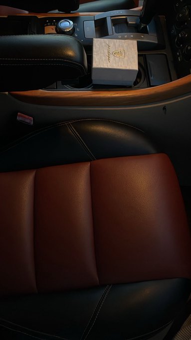 Interior view of a luxury car featuring black and brown leather seats, with a small white box resting on the center console near the gear shifter.
