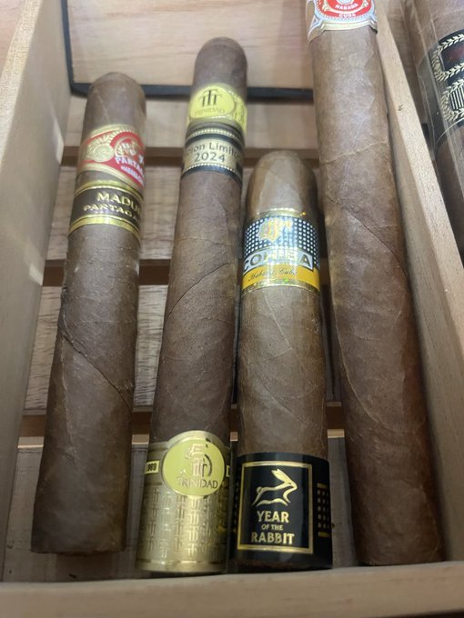 Four cigars rest side by side in a wooden box, with visible bands reading “Madura Pastrana,” “Short Limit 2024,” “Cohiba,” and “Year of the Rabbit,” alongside a $5 Trindad stamp on one cigar. The image pairs a premium cigar selection with the post’s leisurely Yorkshire tea ritual, though the tea and other food mentioned are not shown.