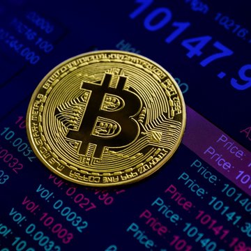 A physical Bitcoin token rests atop a digital display showing a price of 10147.9 with trading volume data, visually reinforcing the article about short-term Bitcoin holders enjoying a 30-day profit streak—a signal CryptoQuant associates with past market recoveries.