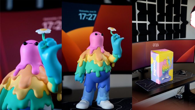 A colorful Doodles collectible figure with a melting rainbow body holding a daisy is displayed on a desk in front of a monitor showing "17:23," with its branded yellow product box sitting beside it, suggesting the owner is curating web2-friendly collectibles with a distinct web3 flair for their "Desk Series."