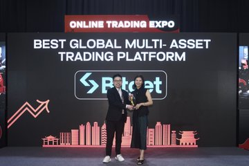 The image features a man and a woman standing together behind a podium, both holding an award. They are positioned in front of a large screen displaying a logo for "Best Global Multi-Asset Trading Platform." The text on the screen reads "Freshly named “Best Global Multi-Asset Trading Platform.” @GracyBitget shared the vision: no more asset silos, just one unified gateway for what comes next." This award is presented to them as a symbol of their achievement and contribution to the platform's success.