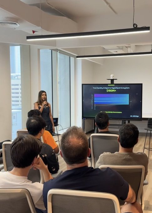 A woman presenting to a seated audience in a modern office space, with a slide displaying 'Total liquidity bridged to Hyperliquid Ecosystem' showing $150M+.