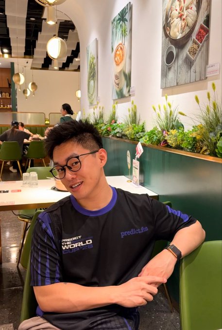 A young man wearing a "PREDICT WORLD CUP" jersey sits smiling in a restaurant, pictured alongside Predict Fun's World Cup merchandise mentioned in the post about betting his remaining $8.16 USDT on a Mexico-England 3:3 draw at 100x odds.