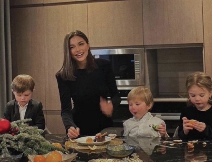 In the image, a woman wearing a black dress stands next to four children who are sitting at a dining table with plates of food in front of them. The scene appears to be set in an indoor kitchen or dining area where they are enjoying their meal together. A microwave is visible on one side of the room, and there's a vase placed nearby as well.

The post seems to be promoting a positive message about the importance of spending quality time with family during special occasions like Christmas. The woman in the image appears to be smiling, which adds warmth and happiness to the scene.