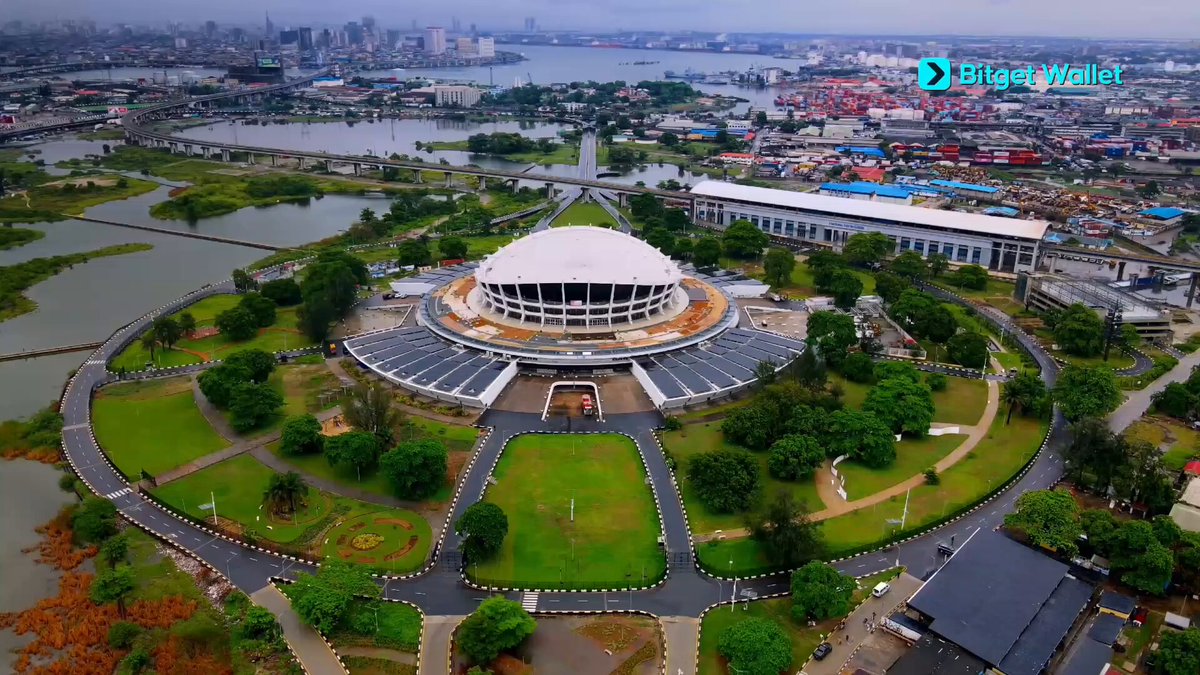 The image features an aerial view of a large circular building with a dome, surrounded by trees and other buildings. The sky above appears cloudy, suggesting that the photo was taken during the day. There are no people visible in the image, but there is text on the picture indicating that it might be related to Bitcoin or cryptocurrency events.
