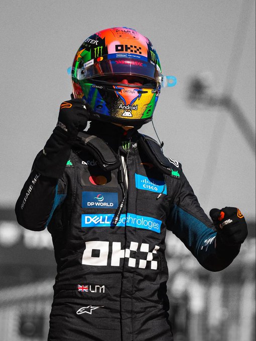 A McLaren F1 driver wearing a vibrant rainbow-colored helmet with "Android" branding and a black race suit featuring "Dell Technologies," "DP World," and "Cisco" sponsor logos raises his fists in celebration, with "LN4" visible on his suit—referencing Lando Norris's car number and his "Papaya" team colors.