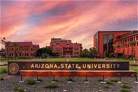 A photograph of the Arizona State University sign at sunset, with brick buildings visible in the background beneath a colorful sky.
