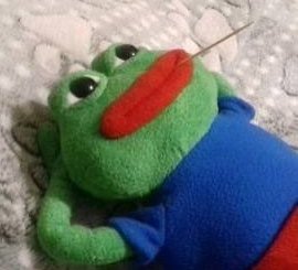 A handmade crochet plush of Pepe the Frog dressed in a blue shirt, lying on a textured white surface.