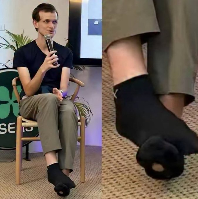 The image shows Vitalik Buterin, Ethereum's co-founder, seated in a chair on stage giving a talk while speaking into a microphone—he is notably wearing socks with a hole in the toe, as highlighted in the close-up on the right. The caption jokes about how despite his immense wealth, he lives minimally, even skipping sock upgrades in favor of staking ETH.