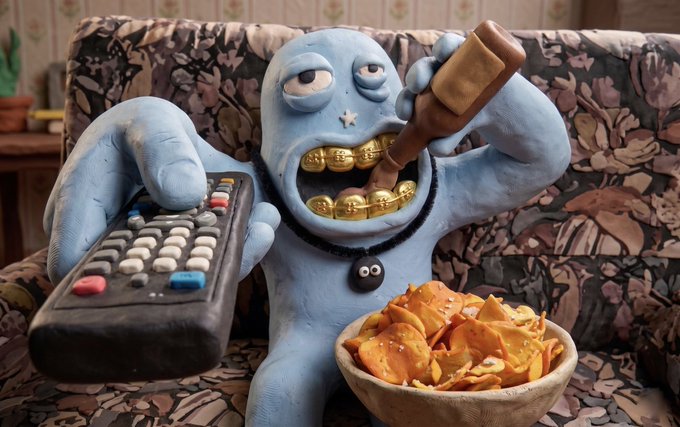 A blue clay sculpture of a creature with gold teeth holding a remote control in one hand and a bottle in the other, sitting on a floral couch next to a bowl of chips.