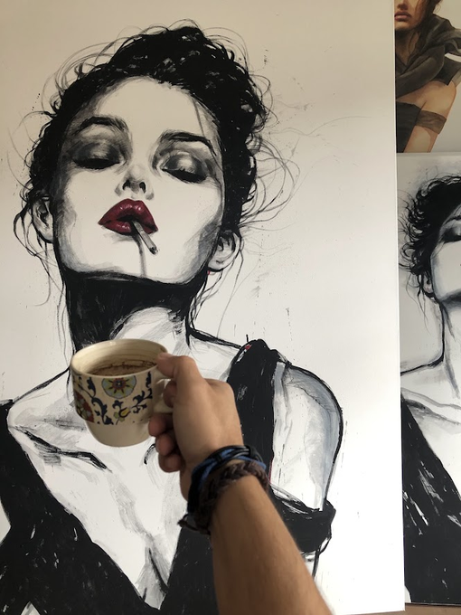 A hand holding a mug poses in front of an ink and charcoal painting of a woman with red lips and a cigarette.