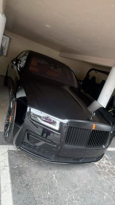A black Rolls-Royce luxury sedan parked in an indoor garage, featuring the iconic Spirit of Ecstasy emblem and the distinctive chrome grille.