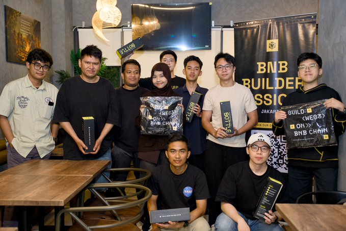 A group of people pose together at what appears to be a BNB Chain (BNB Builders Classic) event, holding branded boxes and merchandise in Jakarta.