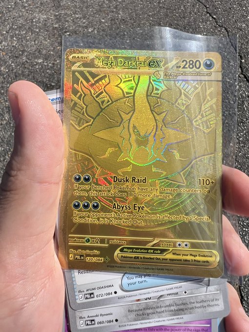 A hand holds a gold Mega Darkrai ex Pokémon trading card (280 HP) with attacks Dusk Raid and Abyss Eye, still in its protective sleeve.