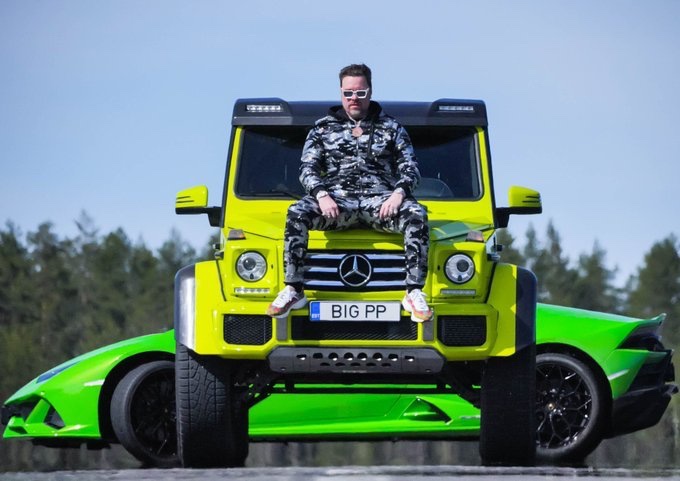 A man in sunglasses and camouflage sits on the hood of a bright yellow Mercedes-Benz G-Wagon, with a green sports car behind it and a license plate reading 'BIG PP'.