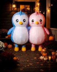 A whimsical scene featuring two penguin characters, one blue and one pink, standing on a cobblestone path decorated with pumpkins and autumn foliage.