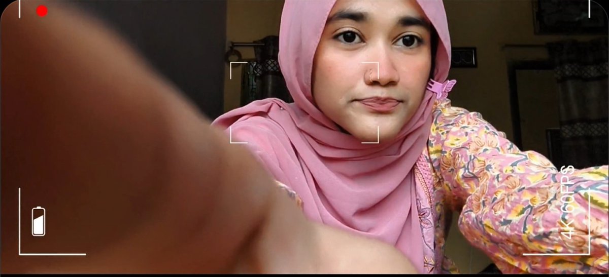 A woman wearing a pink hijab and floral-patterned top takes a selfie-style video, with "4K/60FPS" and a battery indicator visible on screen.

The image appears to be a thumbnail or cover for a video where the creator introduces their analysis of NEAR Protocol's revenue model and tokenomics, contrasting fees with actual revenue and explaining buyback mechanics.