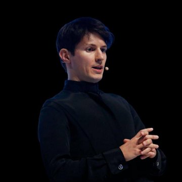 Pavel Durov, the founder of Telegram, speaks at a conference against a black background, wearing a black turtleneck and gesturing with his hands clasped, embodying the defiant stance described in his statement against Russia's "terrorist" designation for refusing to comply with state surveillance demands.