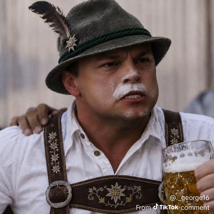 A man with white facial markings wears a traditional Bavarian outfit including an Alpine hat with a feather and edelweiss pin, holding a mug of beer. Text reads '@_george16 From TikTok.com'.