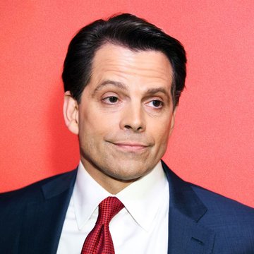A man in a dark suit and red tie makes a skeptical side-glance expression against a red background.