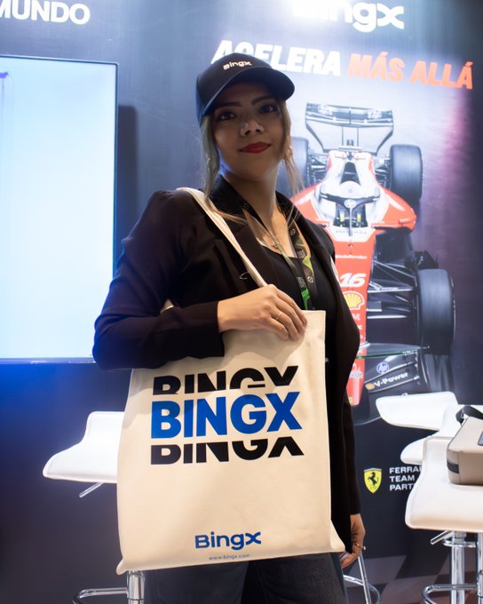 A woman wearing a 'BingX' cap and black blazer holds a BingX tote bag at what appears to be a promotional event, with a Ferrari F1 race car and the text 'ACELERA MÁS ALLÁ' in the background.