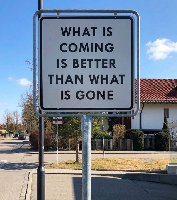 A street sign displays the inspirational quote 'WHAT IS COMING IS BETTER THAN WHAT IS GONE' mounted on a pole in a residential area.