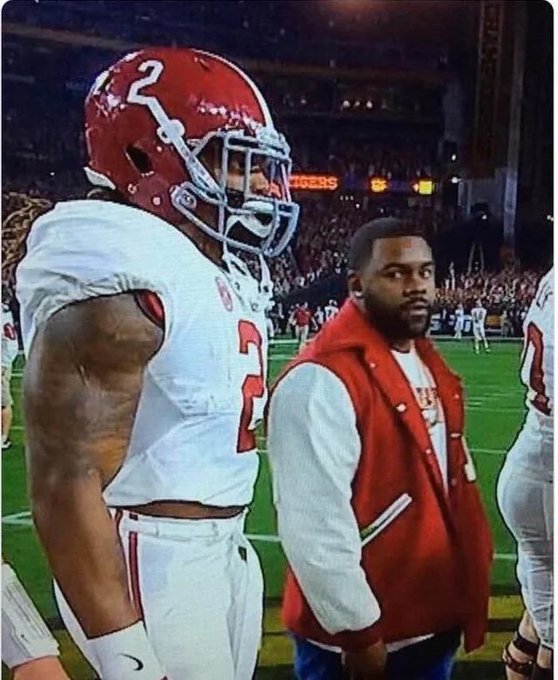 A nighttime football scene featuring an Alabama player in a white #2 jersey and red helmet standing on the field next to a coach or staff member wearing a red letterman jacket.