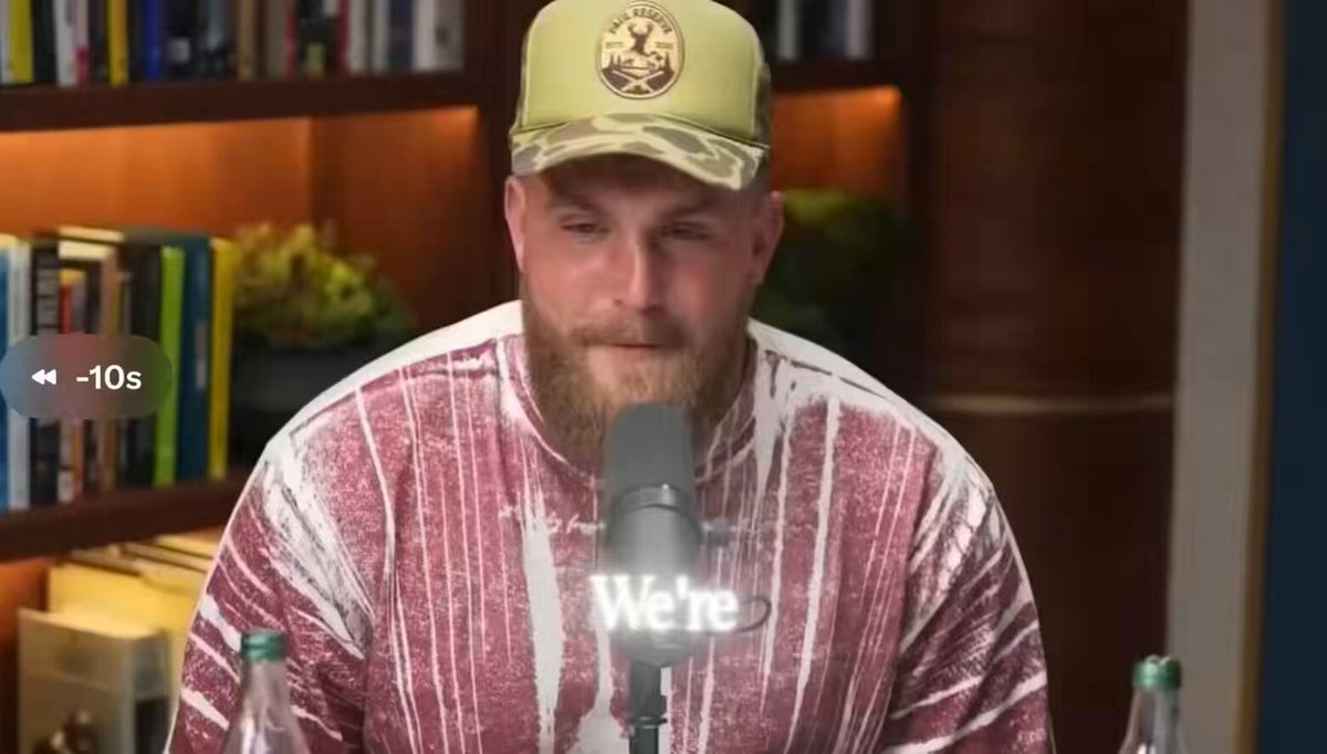 The image features a man wearing a red and white striped shirt with a gold logo sitting at a microphone, likely participating in an interview or podcast discussion. The background includes several bookshelves filled with various books, suggesting that this scene takes place in a library or a similar setting. The caption of the image reads "We're", which could be part of a quote from someone else's post on social media.
