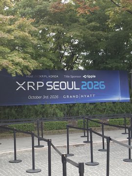 An outdoor banner for the 'XRP Seoul 2026' event hosted by XRP Korea with Ripple, scheduled for October 3rd, 2026 at Grand Hyatt, with stanchions set up in front.
