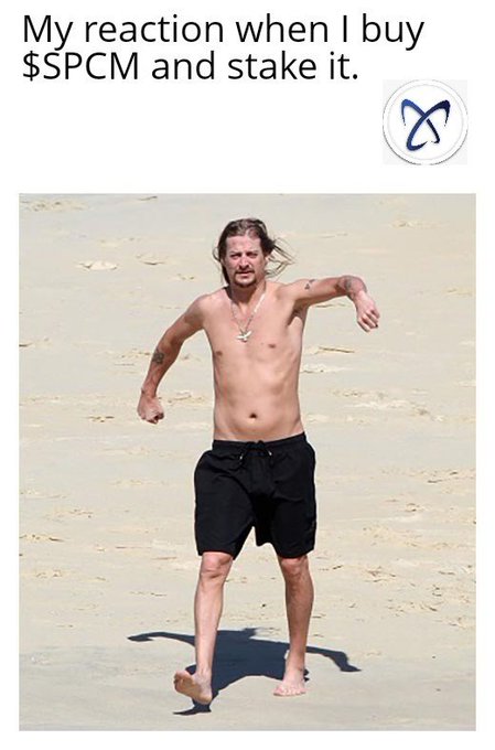 A meme featuring a shirtless, thin man in black swim trunks running awkwardly on a sandy beach, with the caption 'My reaction when I buy $SPCM and stake it.' and a logo in the top right corner.
