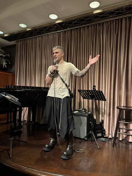 A man stands onstage singing into a microphone with one arm raised, surrounded by a piano, guitar, amplifier, music stand, and floor-to-ceiling curtains. The image accompanies a post thanking attendees for coming to a Solana trading mixer and Alpenglow countdown in Hong Kong.