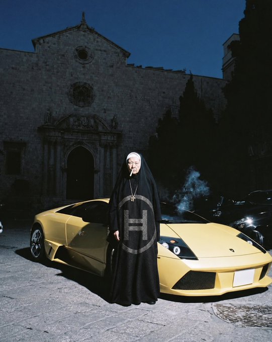 Surreal fashion photograph of a person dressed as a nun holding a cigarette while standing in front of a yellow Lamborghini, with a gothic stone building in the background.