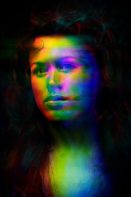 An artistic portrait of a woman's face illuminated by vibrant rainbow-colored lighting against a dark background.
