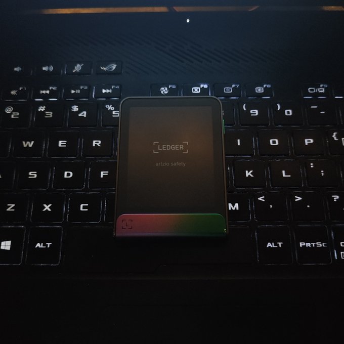 A Ledger hardware cryptocurrency wallet displayed on a laptop keyboard, showing the 'LEDGER' logo and the message 'artzio safety'.