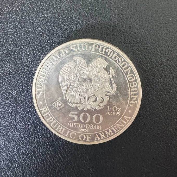 A 1 oz .999 fine silver commemorative coin from the Republic of Armenia featuring the national coat of arms, valued at 500 Dram, dated 2024, photographed against a dark textured surface.