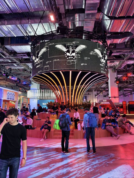 A giant suspended LED installation featuring an eagle emblem dominates the Sui Network booth on the B2 floor of the venue, drawing a crowd of attendees who gather on the tiered wooden seating beneath its glowing display.