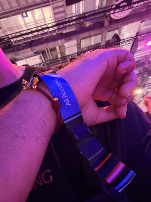 A close-up of a wrist wearing a blue 'All Access' event wristband and a beaded bracelet, taken at what appears to be a concert or event venue.