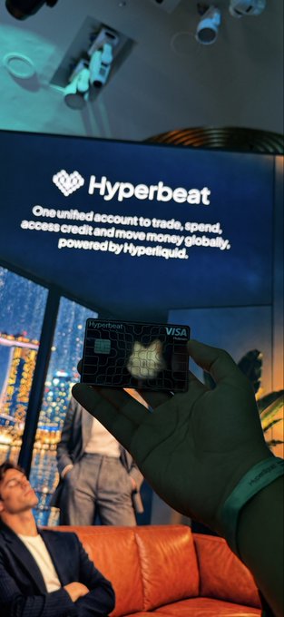 A hand holding a black Hyperbeat VISA card in front of a TV screen displaying the Hyperbeat logo and tagline 'One unified account to trade, spend, access credit and move money globally, powered by Hyperliquid.'