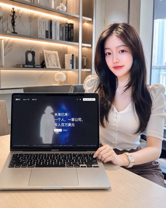 A young woman sitting at a desk with a MacBook Air displaying the OKX website and a banner reading '未来已来：一个人，一家公司，年入百万美元' (The future is here: one person, one company, earning millions annually), set in a modern office with bookshelf background.