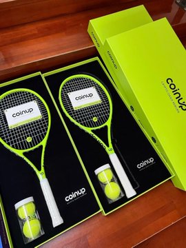 Two neon green "coinup" branded tennis rackets with matching tennis balls are displayed in their branded packaging alongside a CoinUp promotional box, visually showcasing the prize offered in the social media giveaway promotion.