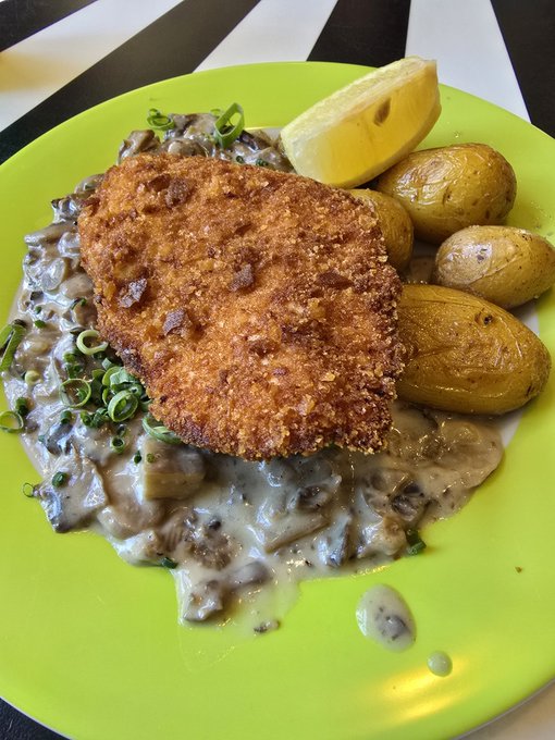 A breaded cutlet rests on a bed of creamy mushroom sauce, accompanied by roasted baby potatoes and a lemon wedge on a bright green plate. The image showcases a homemade meal, likely shared as a personal achievement while discussing the 25 $Sui transaction in the post.