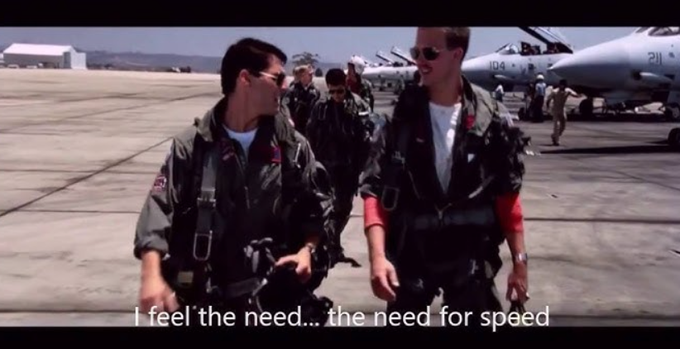 A scene from the movie Top Gun featuring two pilots in flight suits walking on an airfield with fighter jets in the background, captioned 'I feel the need...the need for speed.'