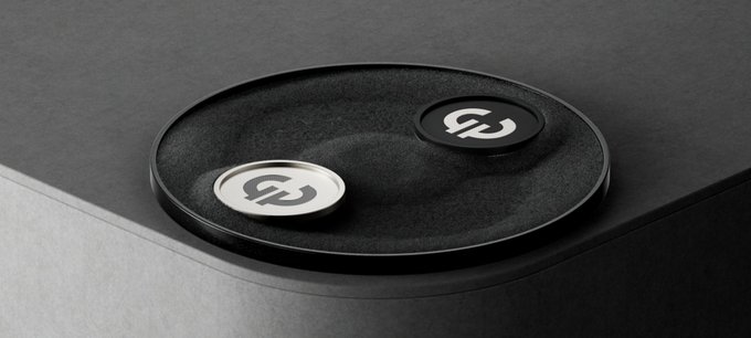Two small black circular tokens with a white 'S' logo rest on a black tray atop a dark, textured surface.