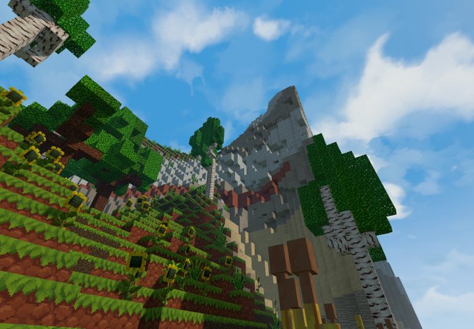 A screenshot from the video game Minecraft showing a grassy blocky landscape with trees and a grey stone mountain under a blue sky with clouds.
