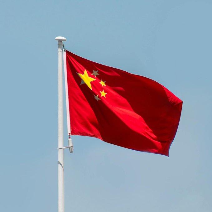 The flag of China, featuring a large yellow star and four smaller stars on a red background, waves against a clear blue sky from a white flagpole.