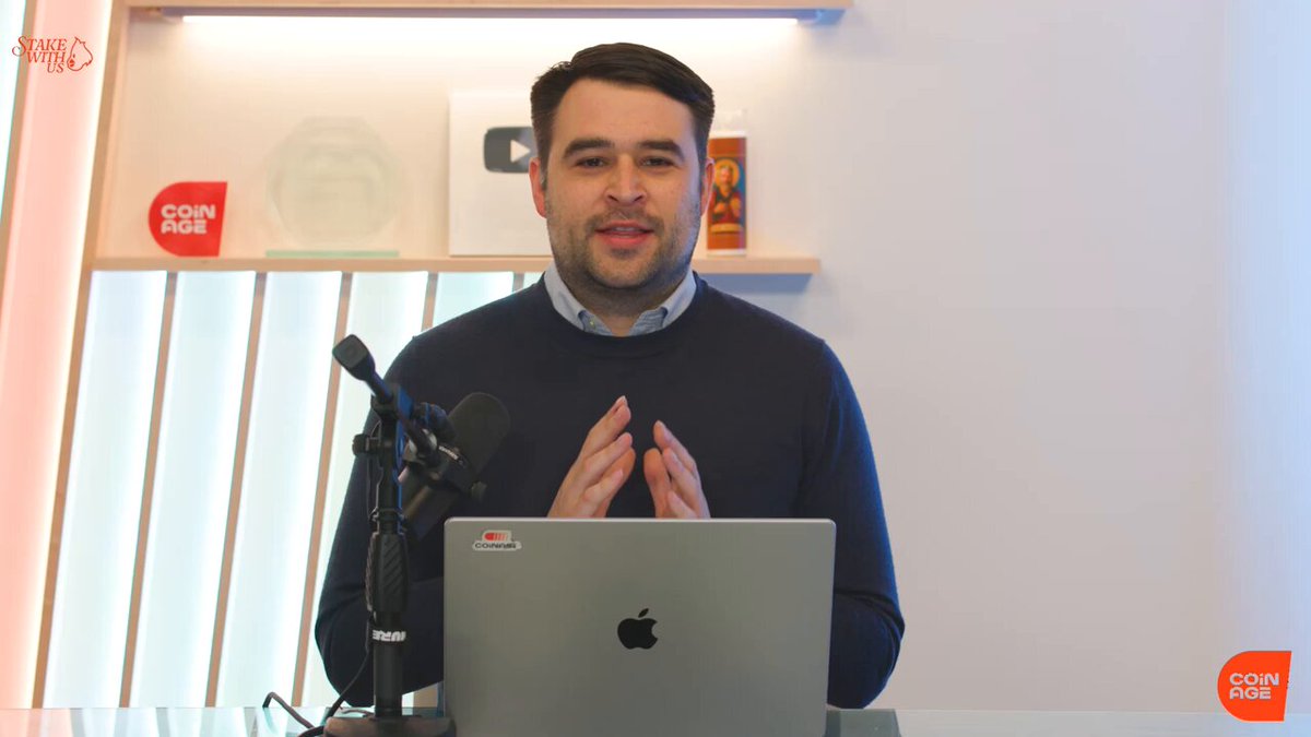A man in a dark sweater sits behind an Apple laptop with a microphone, in a studio setting featuring a YouTube silver play button plaque, a "COIN AGE" sign, and a "Stake with" logo in the corner. The image serves as a throwback to a previous video where he warned that Strategy's $BTC machine was "about to work in reverse," which has since proven prescient given Bitcoin's 27% drop, $MSTR's 53% decline, and $STRC's 22% loss mentioned in the post.